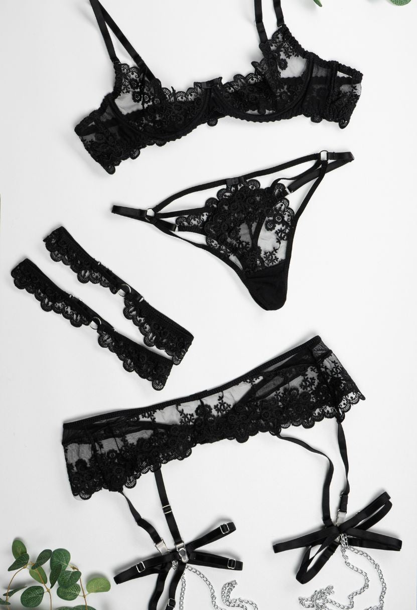 Erotica black lace lingerie set flat lay with bra, thong, garter belt, and leg garter