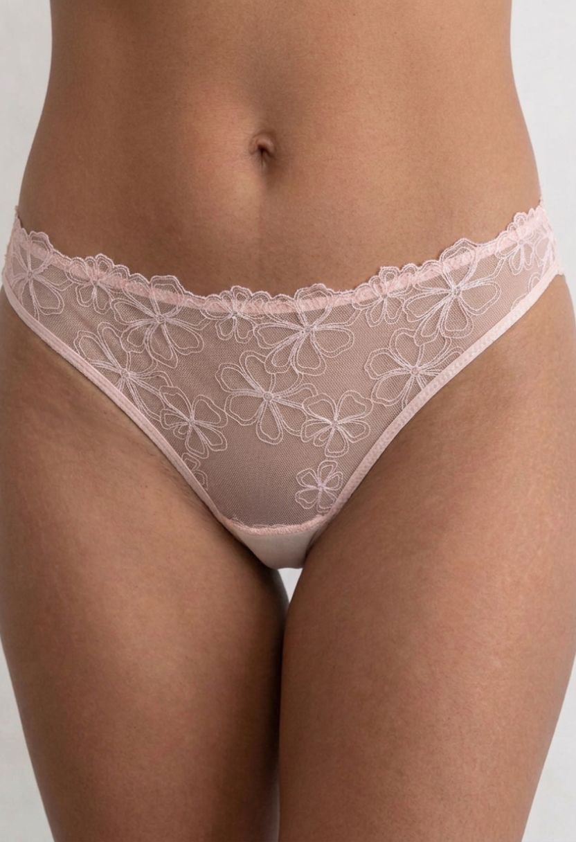 A close-up of a model wearing light pink lace panties with a floral pattern and scalloped trim.