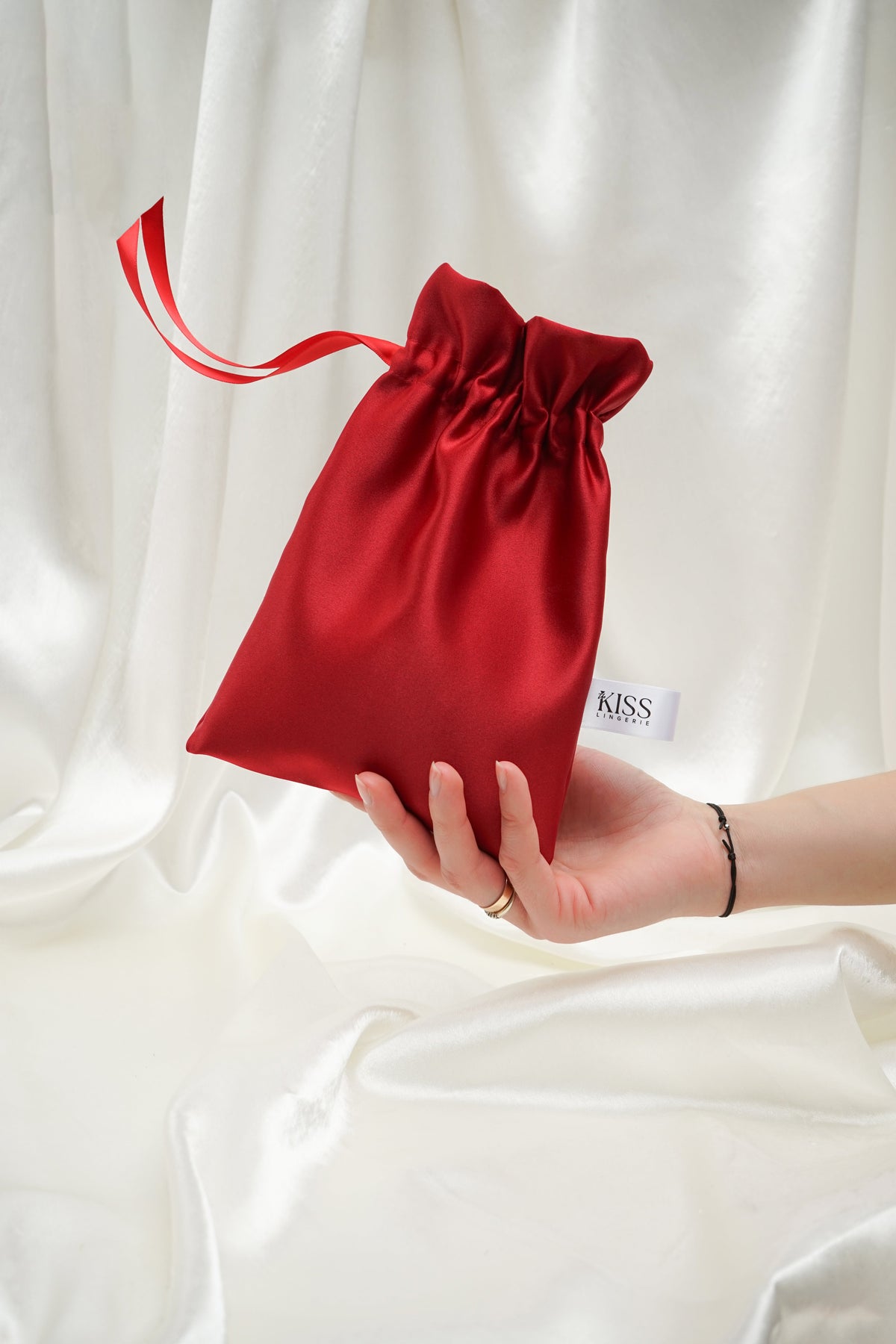 Red satin drawstring gift bag with TheKiss tag held in hand