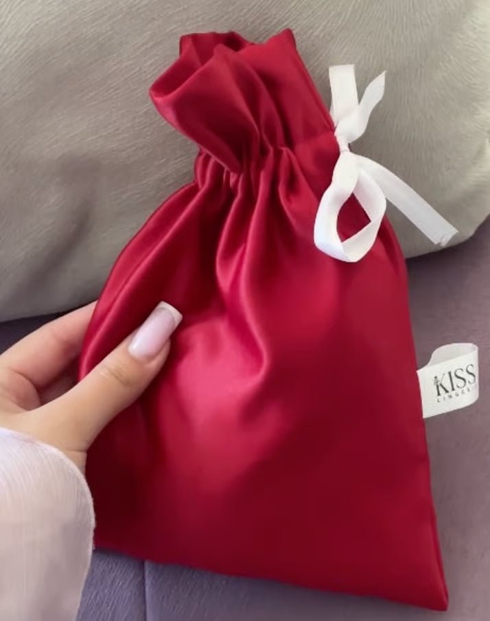 Red satin drawstring gift bag with white ribbon tie held in hand